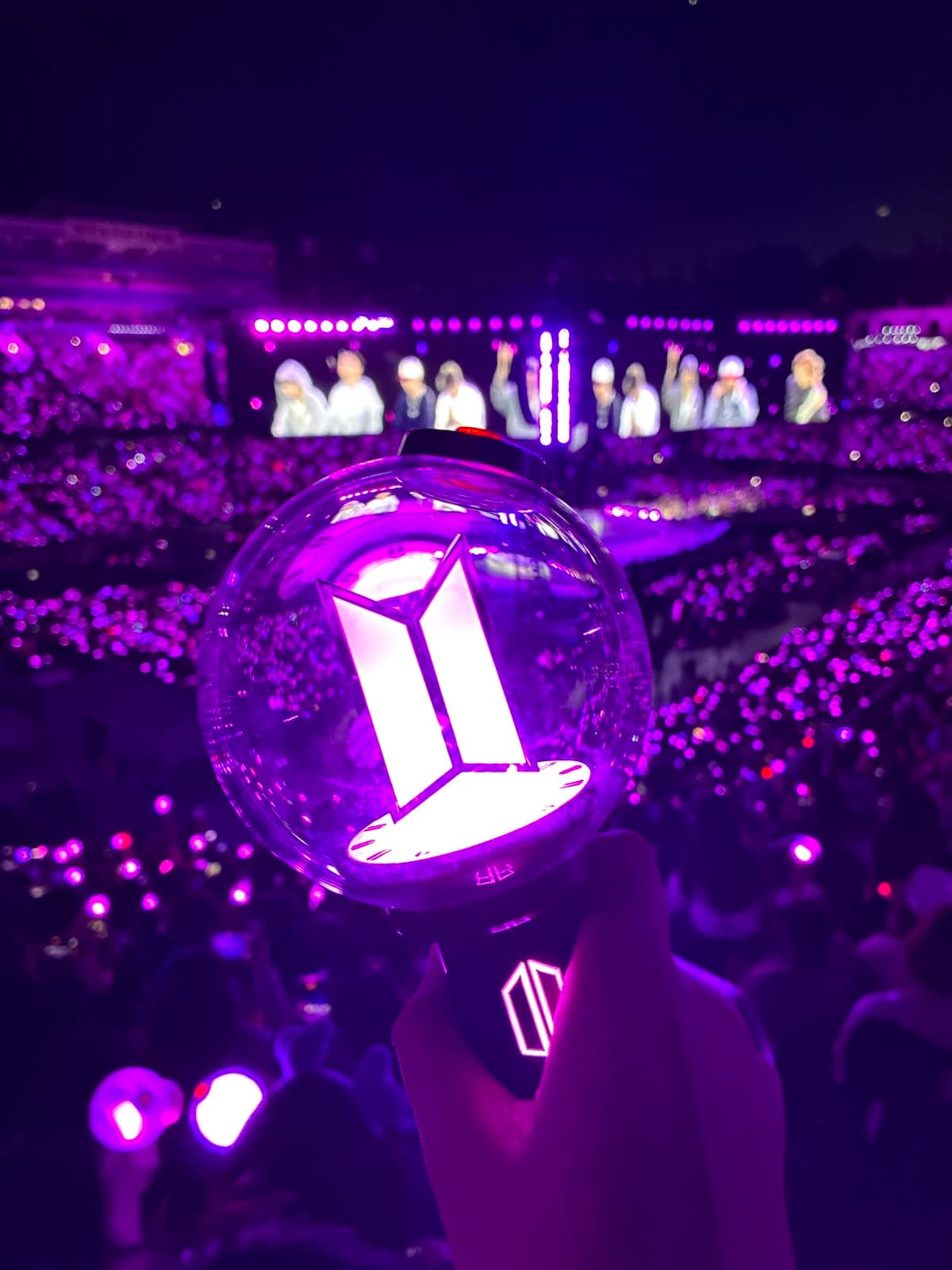 Un ARMY Bomb acceso in mano a una fan durante un concerto, con lo stadio illuminato di viola