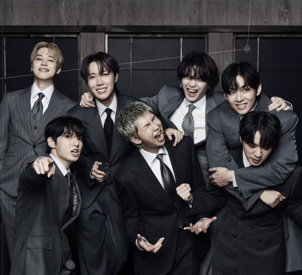 I sette membri dei BTS in abito scuro, sorridenti e abbracciati
